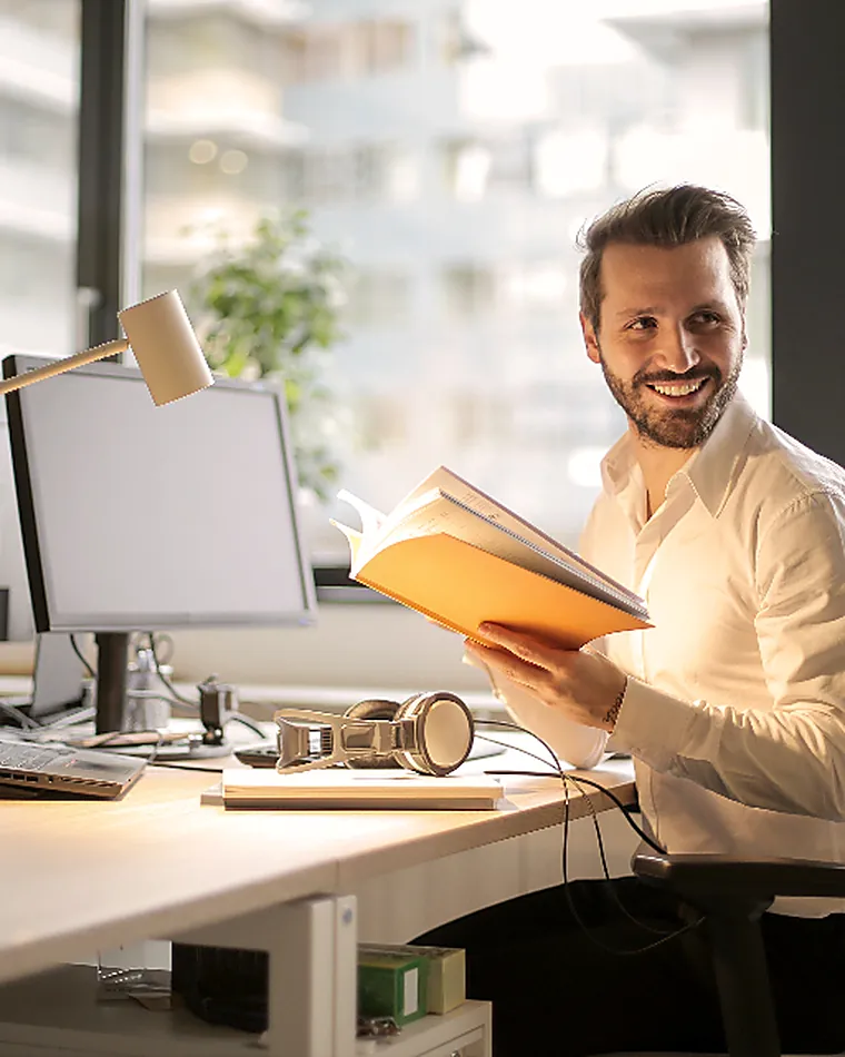 A person reading at a desk beside a window