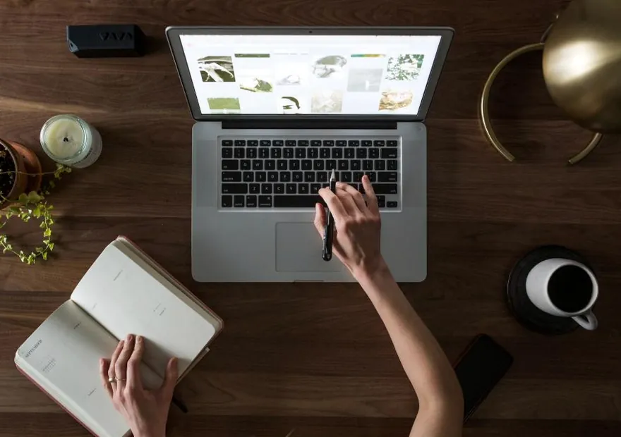 A desk from above with a laptop, notebook and coffee