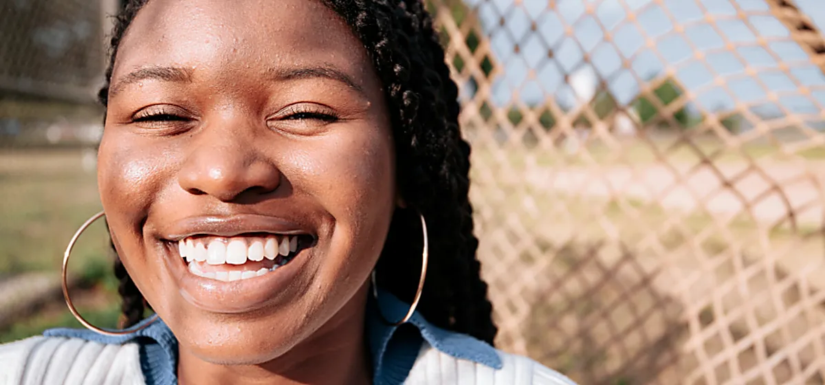 A woman smiling in daylight against a fence